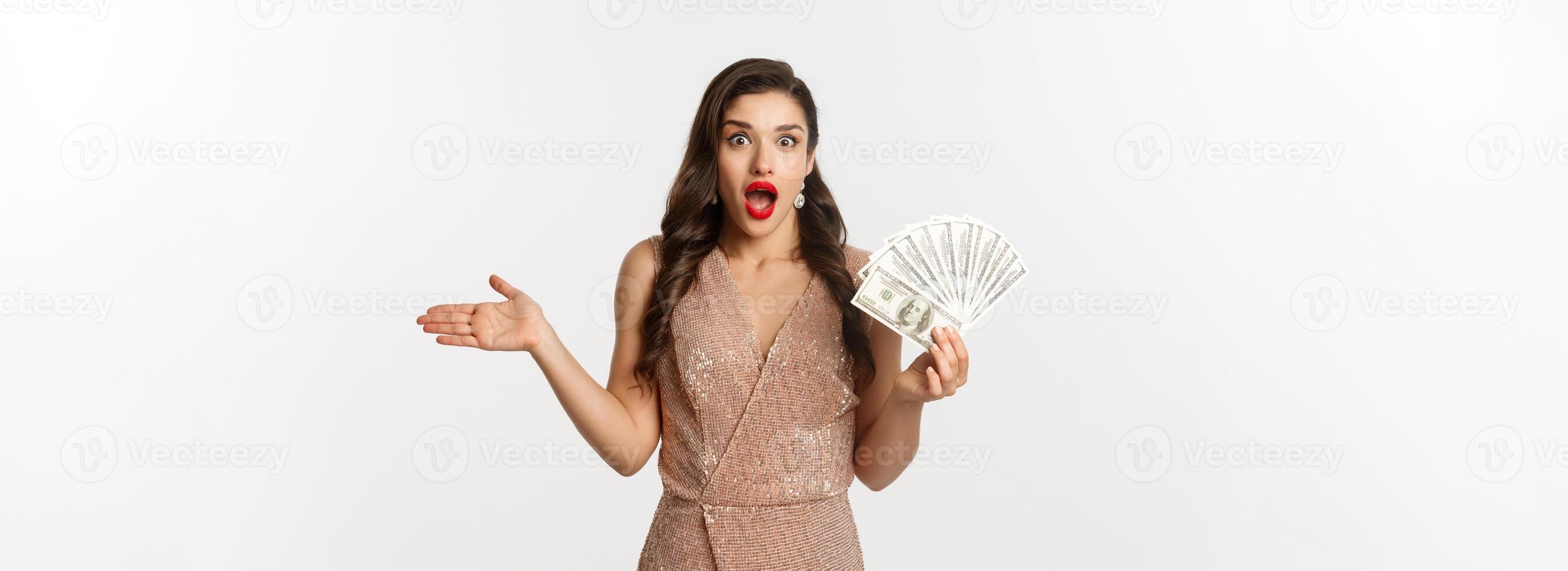 Shopping concept. Elegant woman in glamour dress holding money and looking surprised. winning prize, standing over white background photo