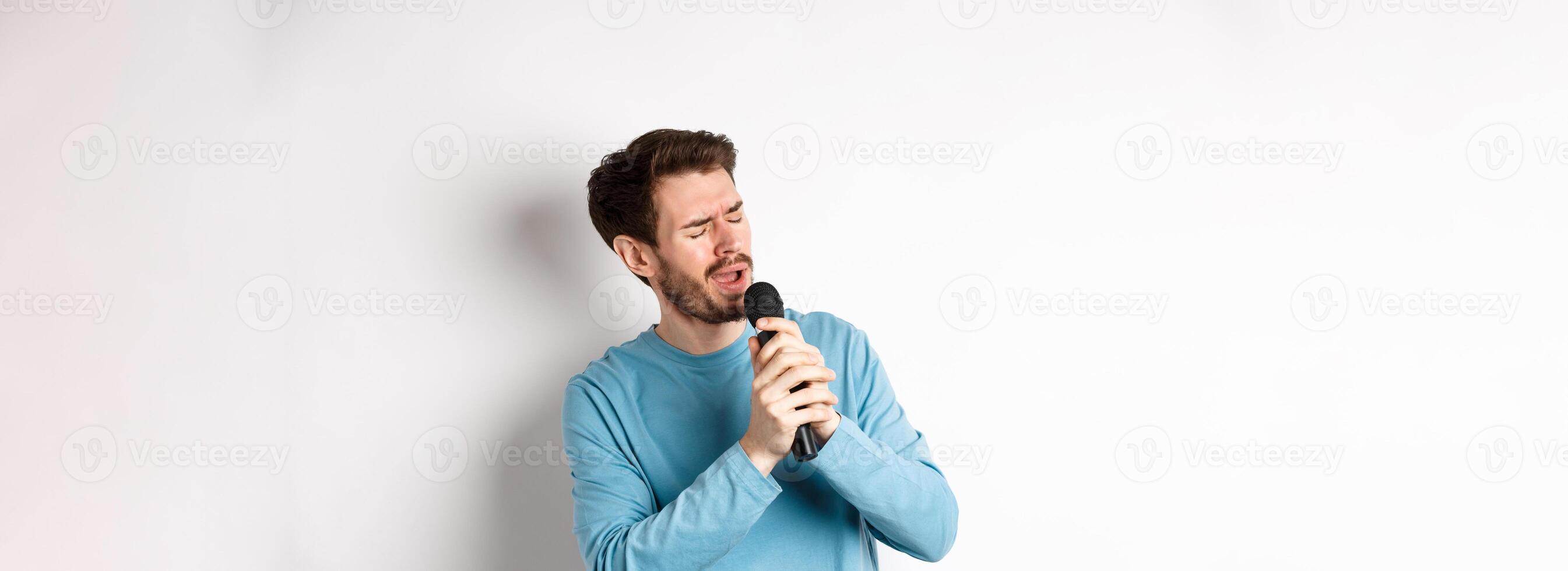 Romantic man singing song in microphone at karaoke, standing over white background photo