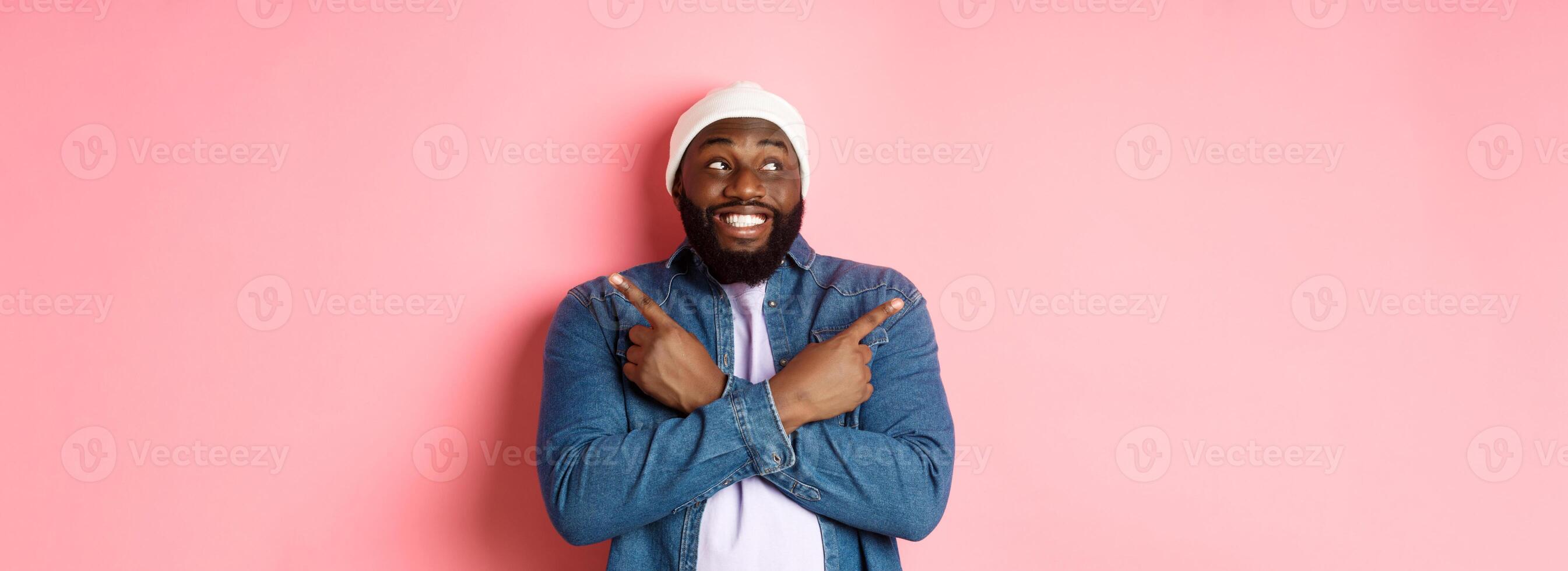 Excited young african-american man pointing sideways, showing two choices and making decision, smiling happy, standing over pink background photo