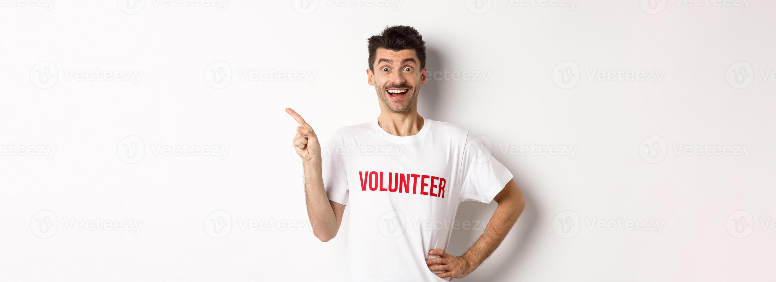 Happy smiling volunteer pointing finger left at copy space, showing announcement, white background photo