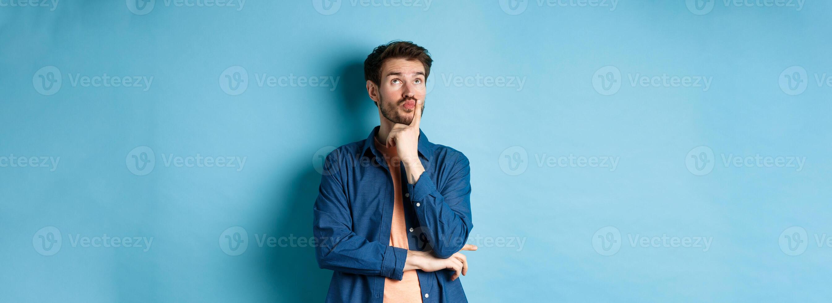 Thoughtful handsome guy making plan, looking up pensive, imaging things, standing on blue background photo