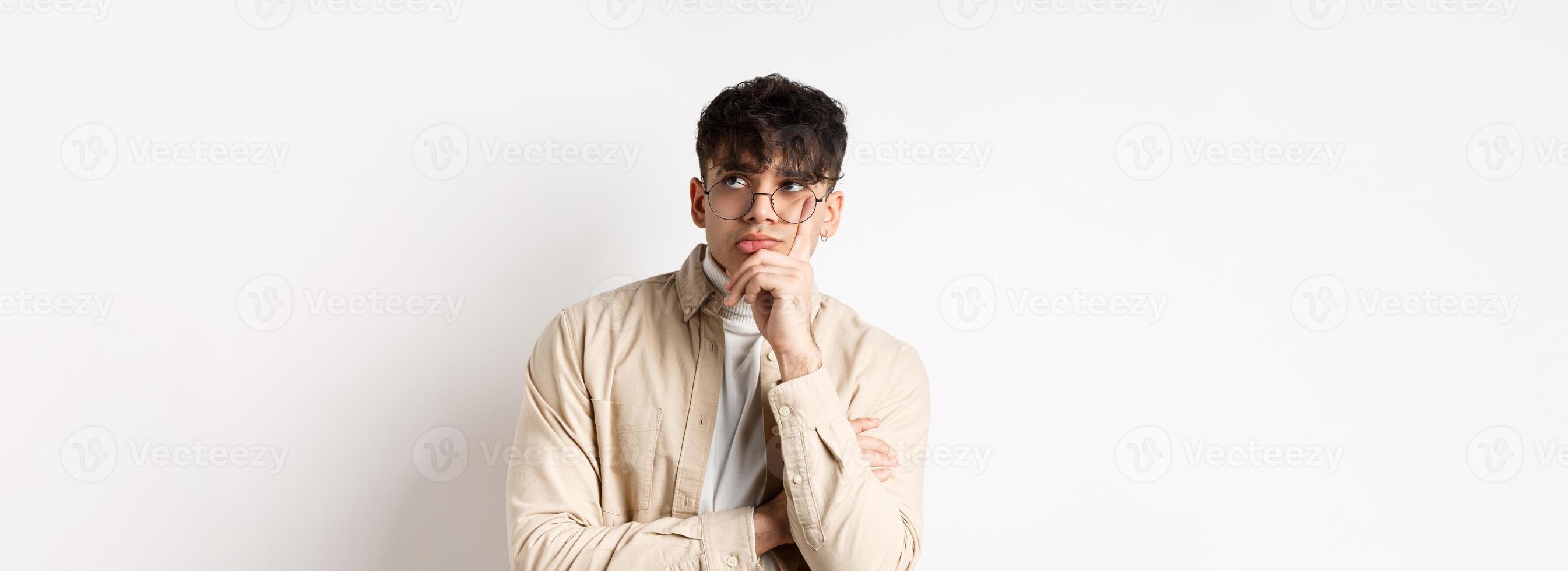 Sad and lonely young man looking at empty space with distressed face, standing thoughtful on white background photo