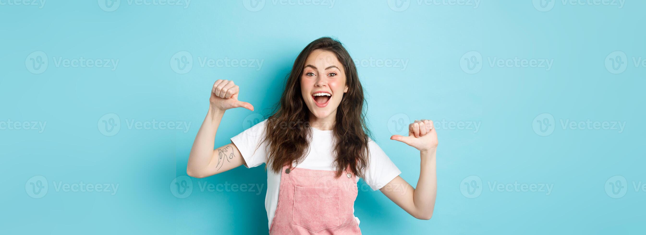 Pick me. Cheerful young girl pointing at herself and smiling, self-promoting, volunteering, looking joyful at camera, standing against blue background photo