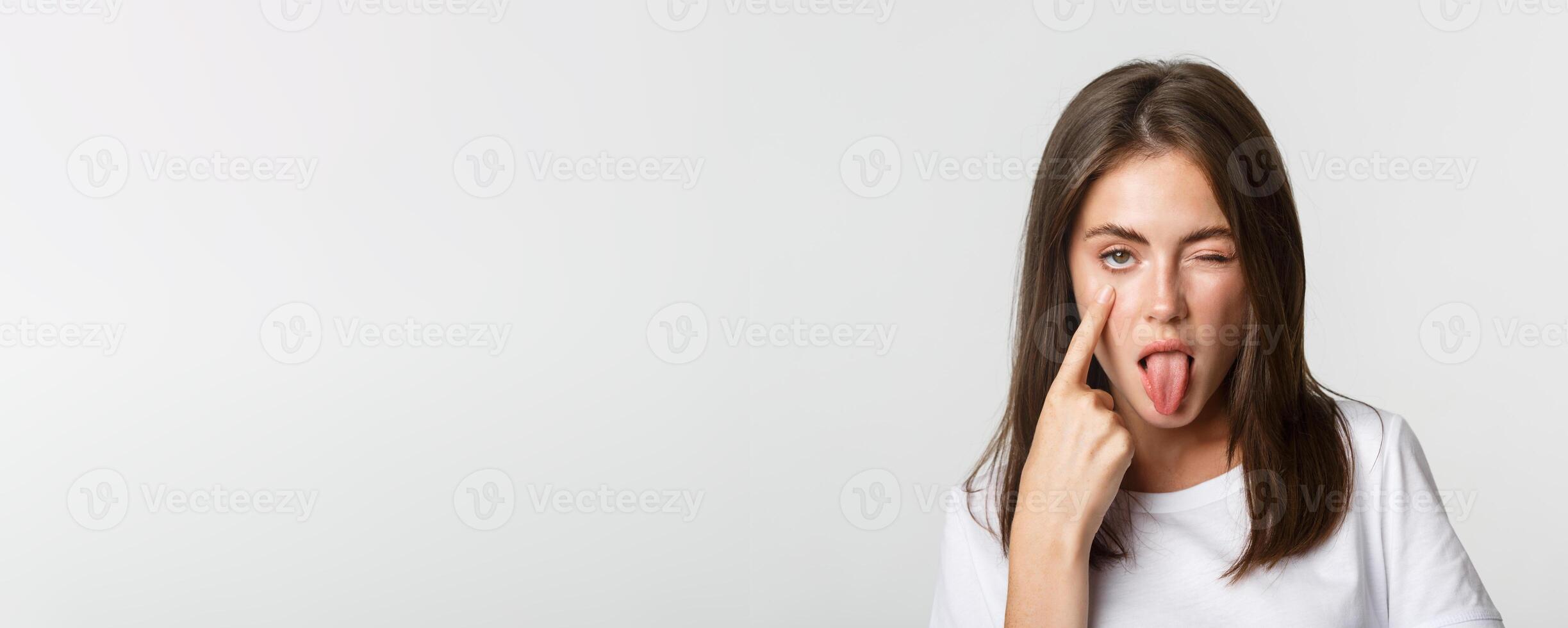 Close-up of silly attractive young girl showing tongue and pulling eyelid, watching you photo