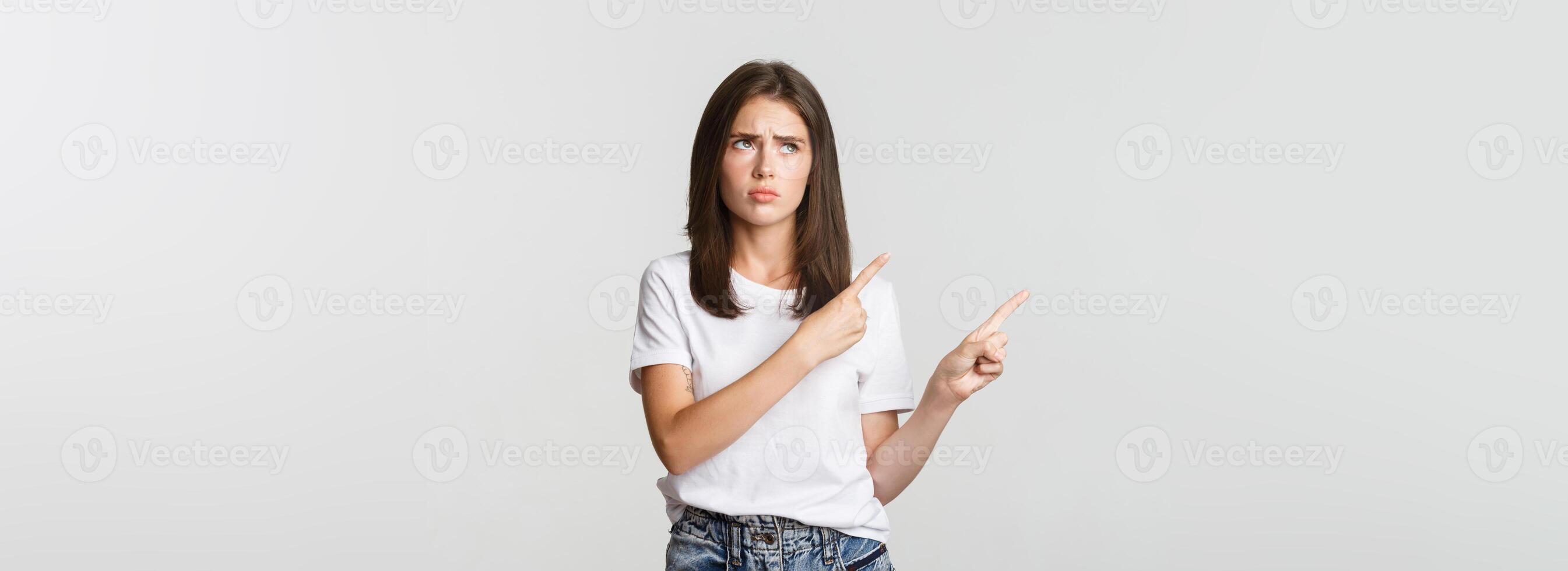 Upset cute girl pointing upper left corner, express regret photo