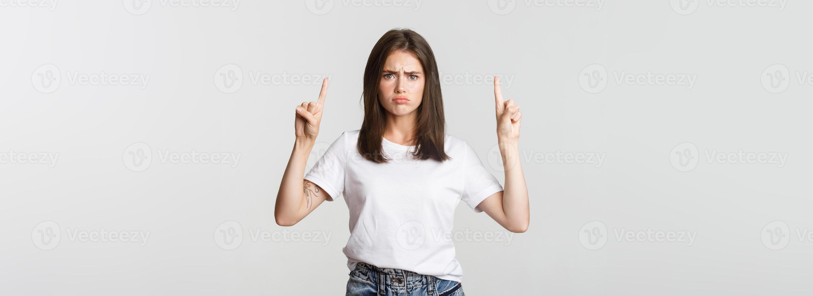 Sulking timid girl pointing fingers up, feeling upset photo