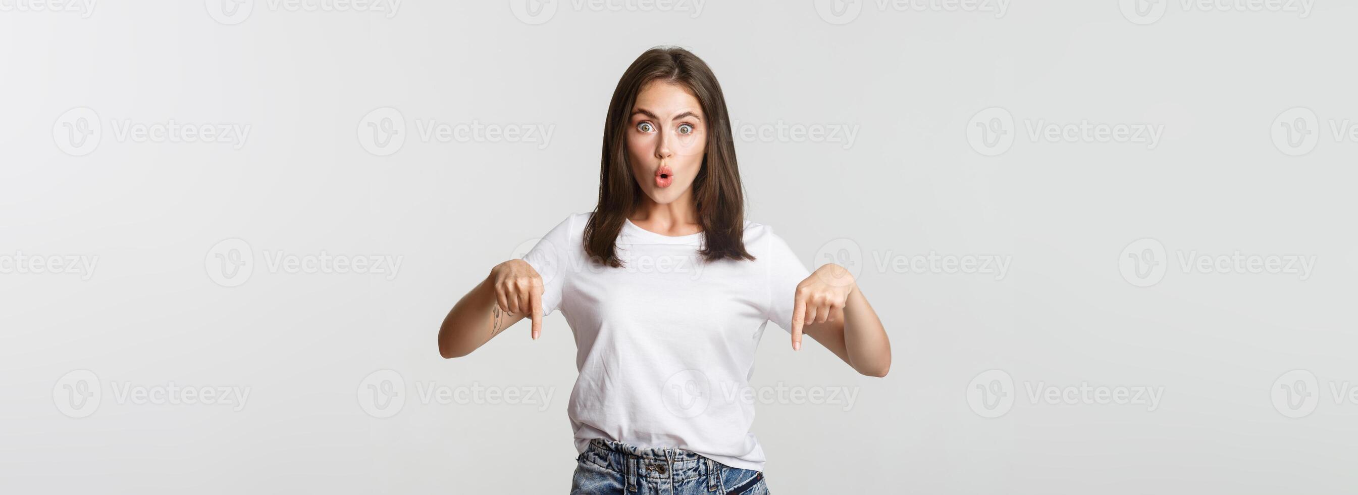 Surprised and impressed brunette girl looking amazed and pointing fingers down photo