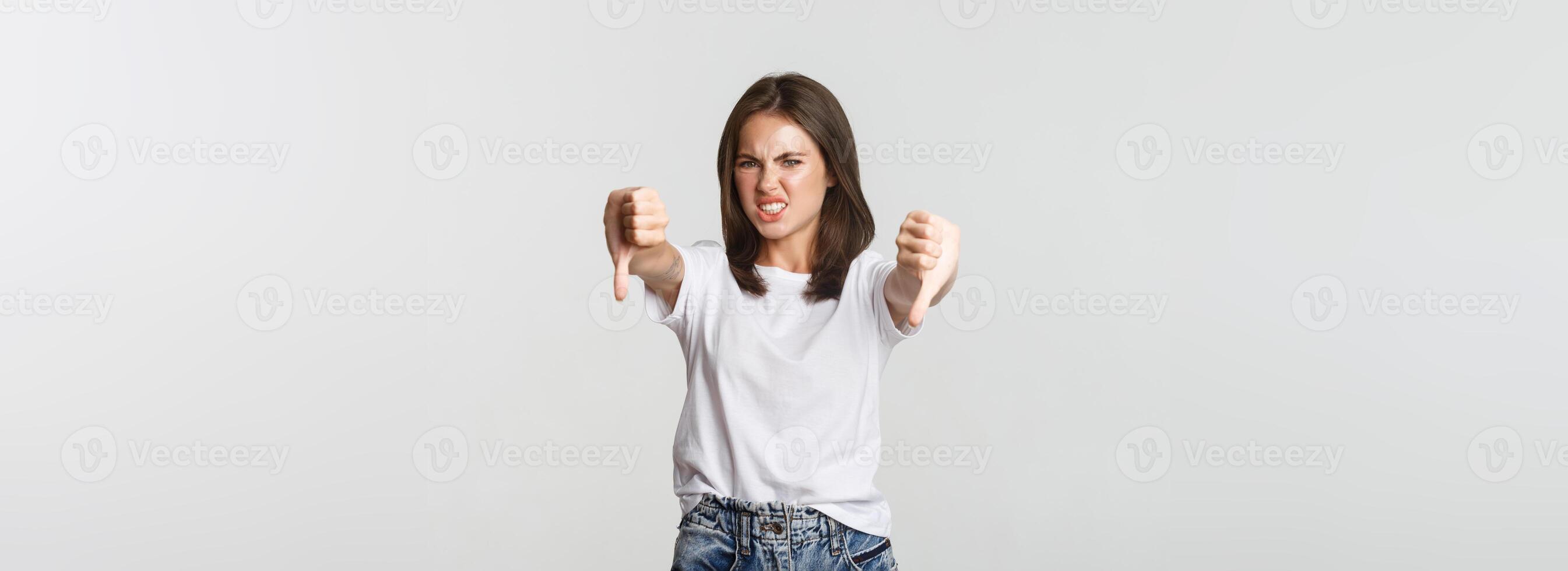 Disgusted brunette girl grimacing from dislike and showing thumbs-down photo
