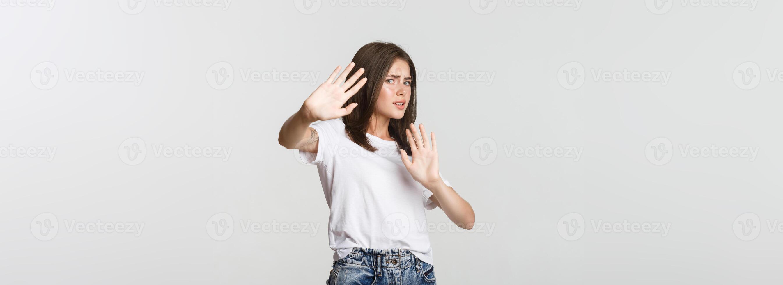 Scared and insecure cute girl raising hands in stop gesture, defending herself photo
