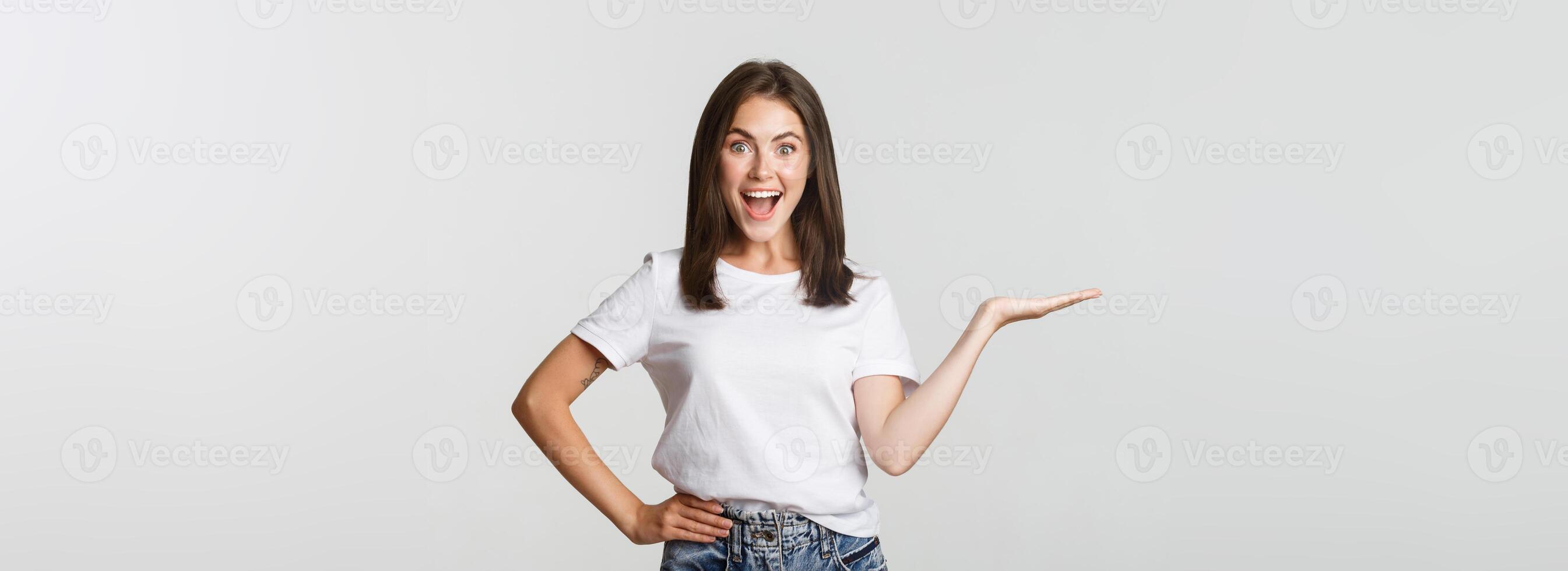 Excited beautiful girl extend arm, holding something on hand and looking happy photo