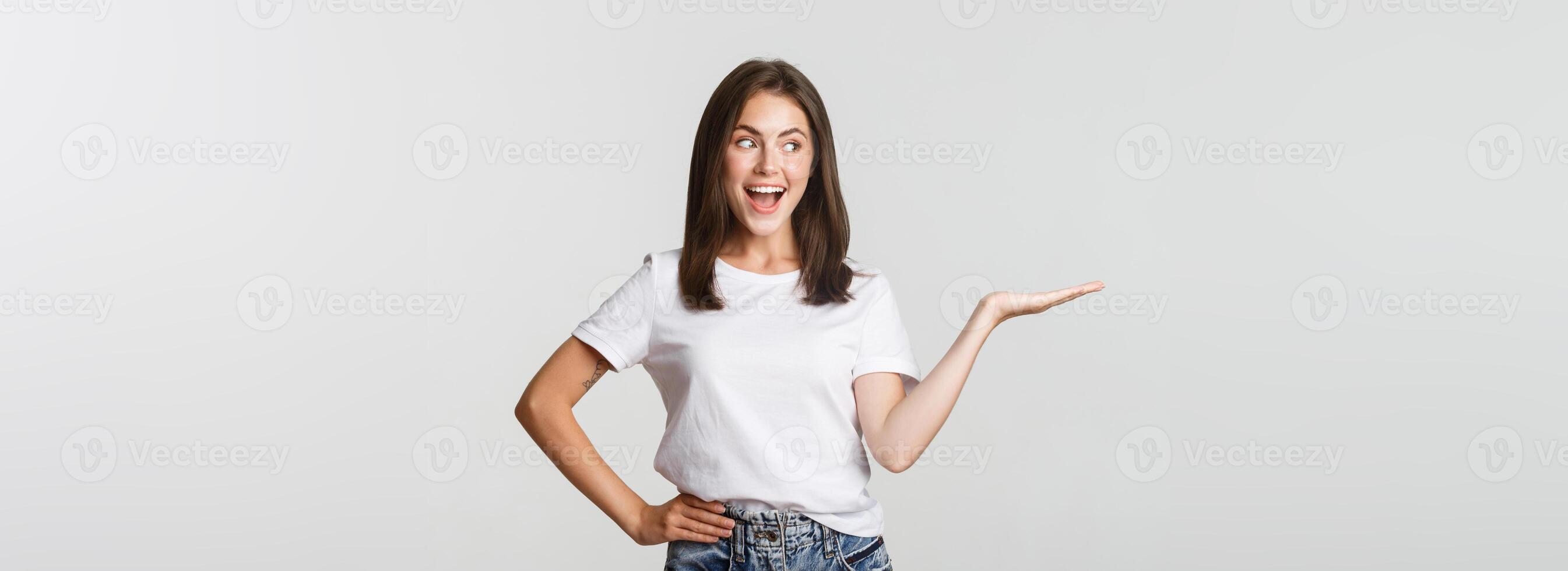 Excited beautiful girl extend arm, holding something on hand and looking happy photo