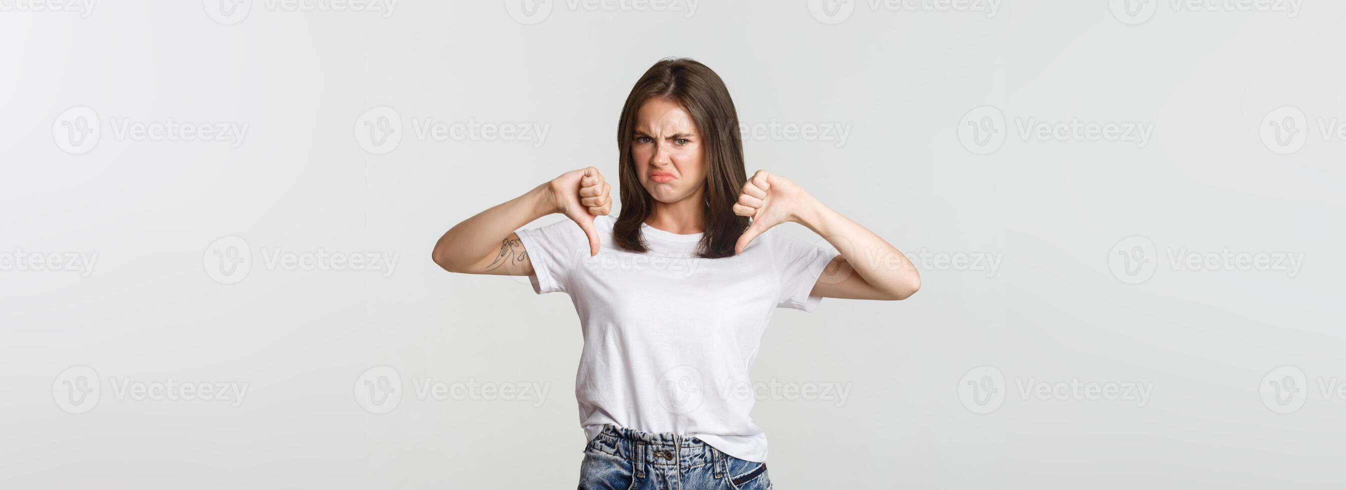 Disappointed grimacing cute girl showing thumbs-down, express dislike photo