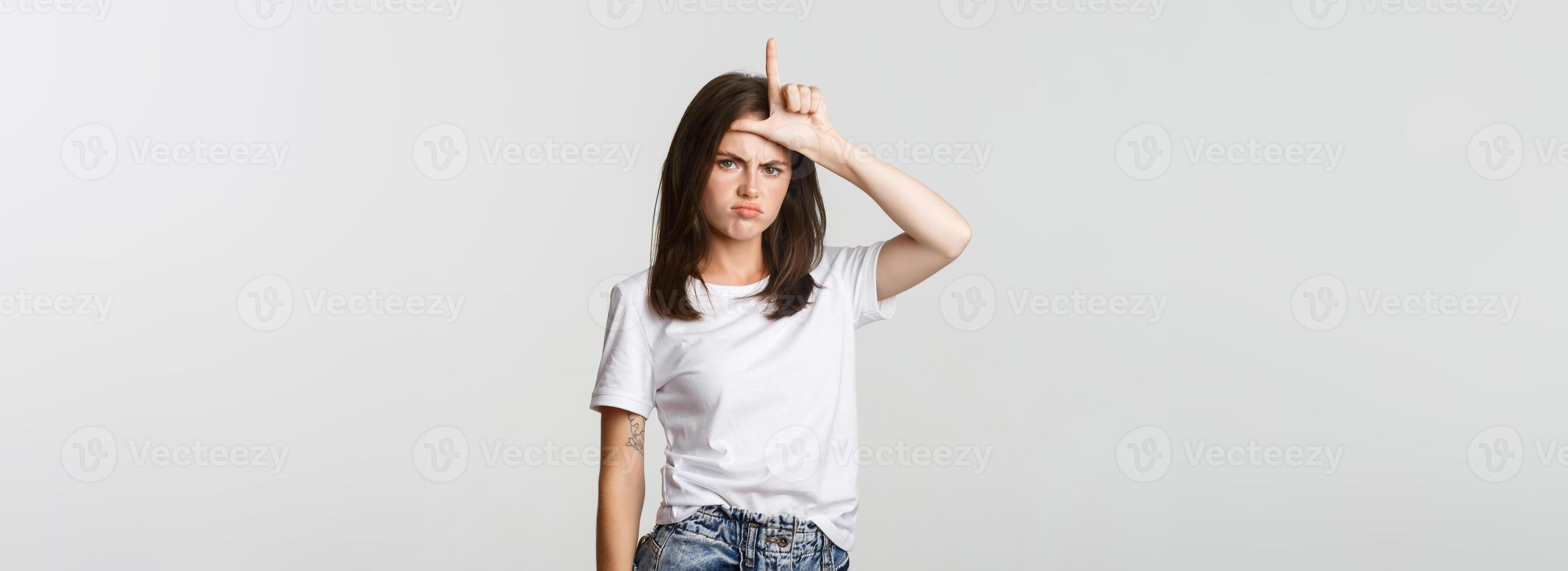 Sad and disappointed brunette girl showing loser gesture and sulking, white background photo