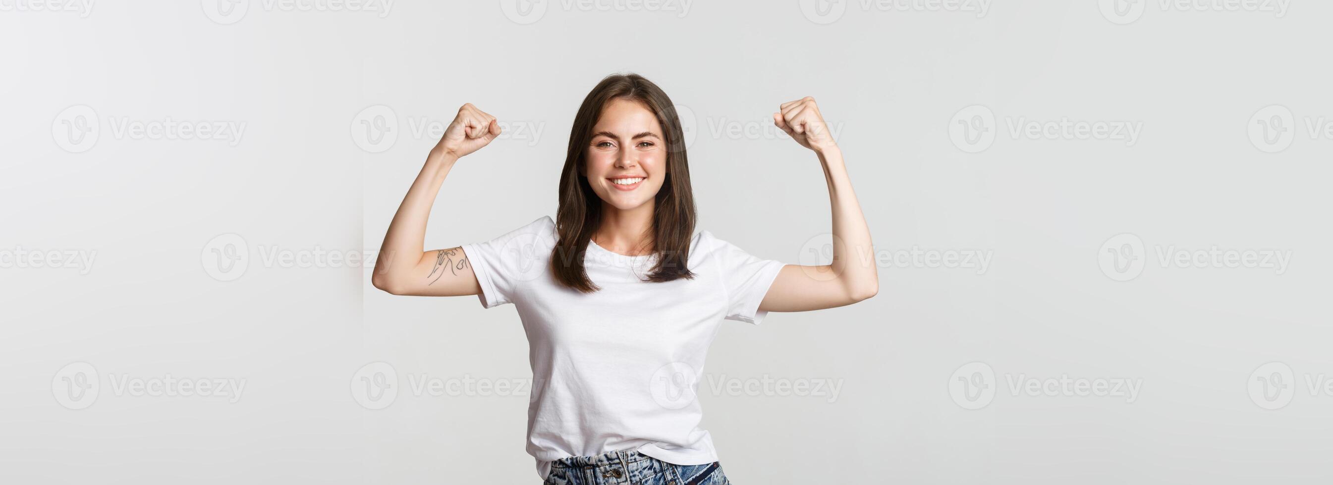Portrait of confident attractive girl flex biceps to show strengths, smiling sassy photo