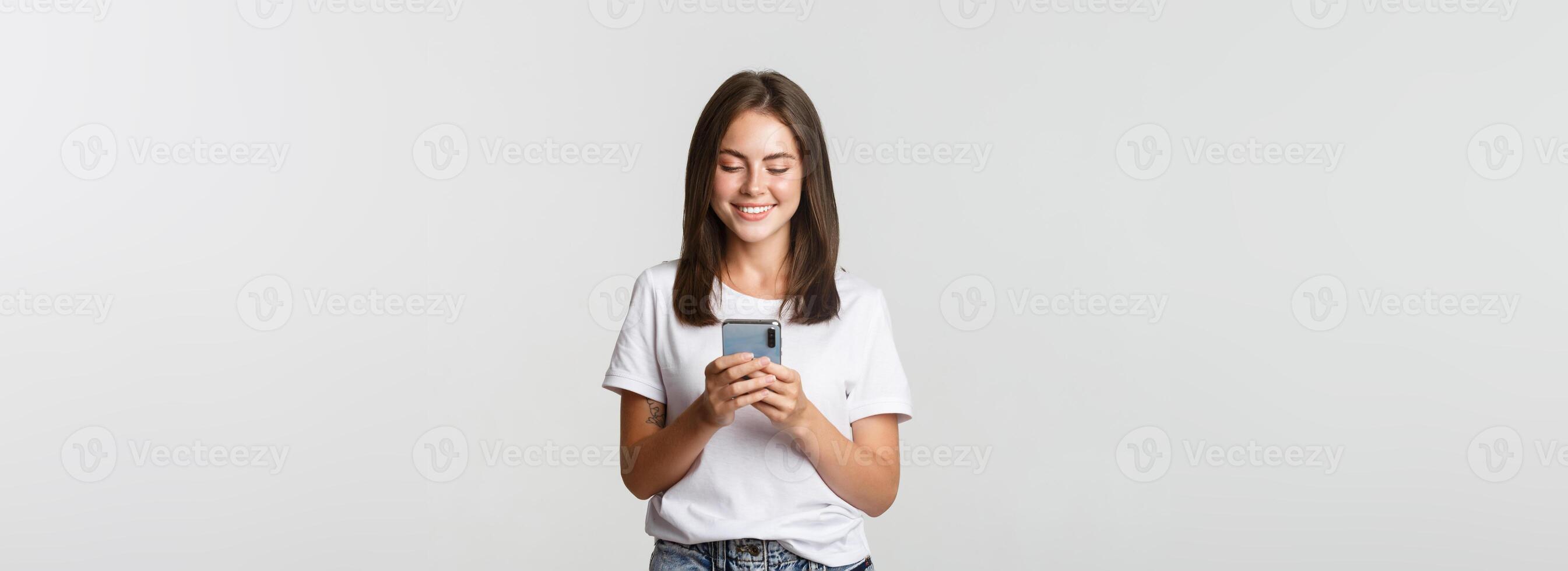 Smiling attractive girl using mobile phone and looking at screen pleased photo