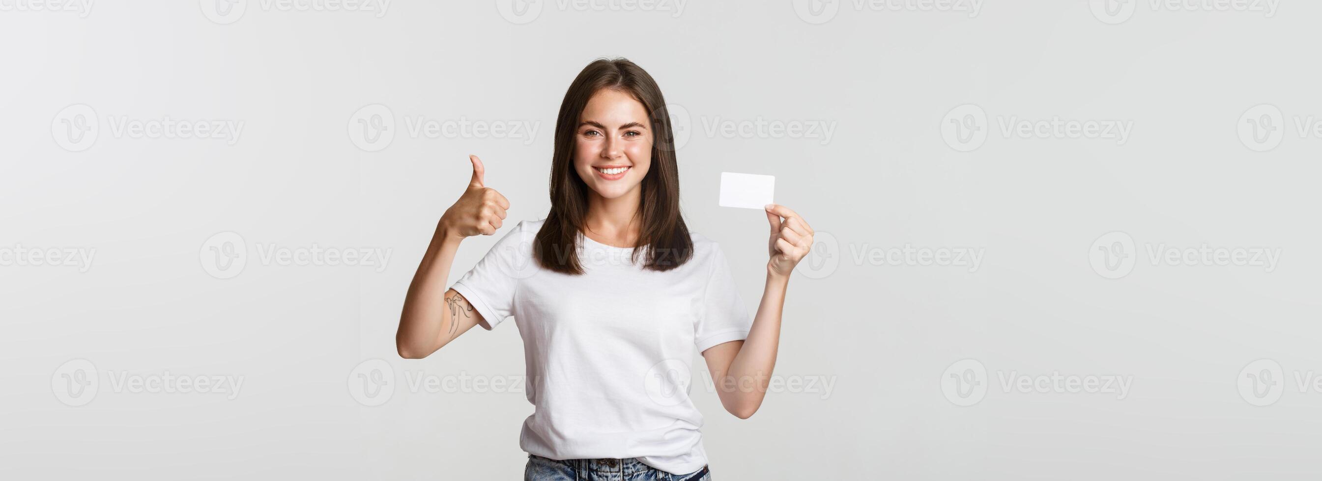 Satisfied attractive girl showing credit card and thumbs-up photo