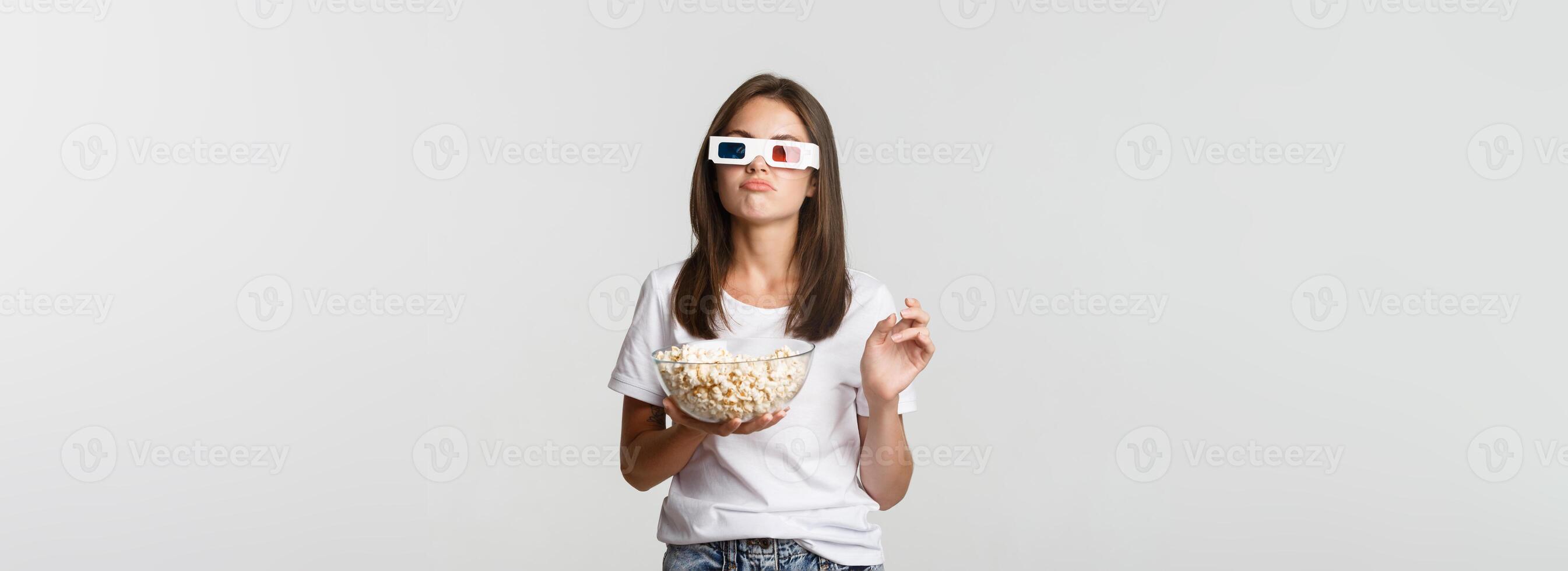 Skeptical beautiful woman in 3d glasses, holding popcorn and looking perplexed, thinking while watching movie photo