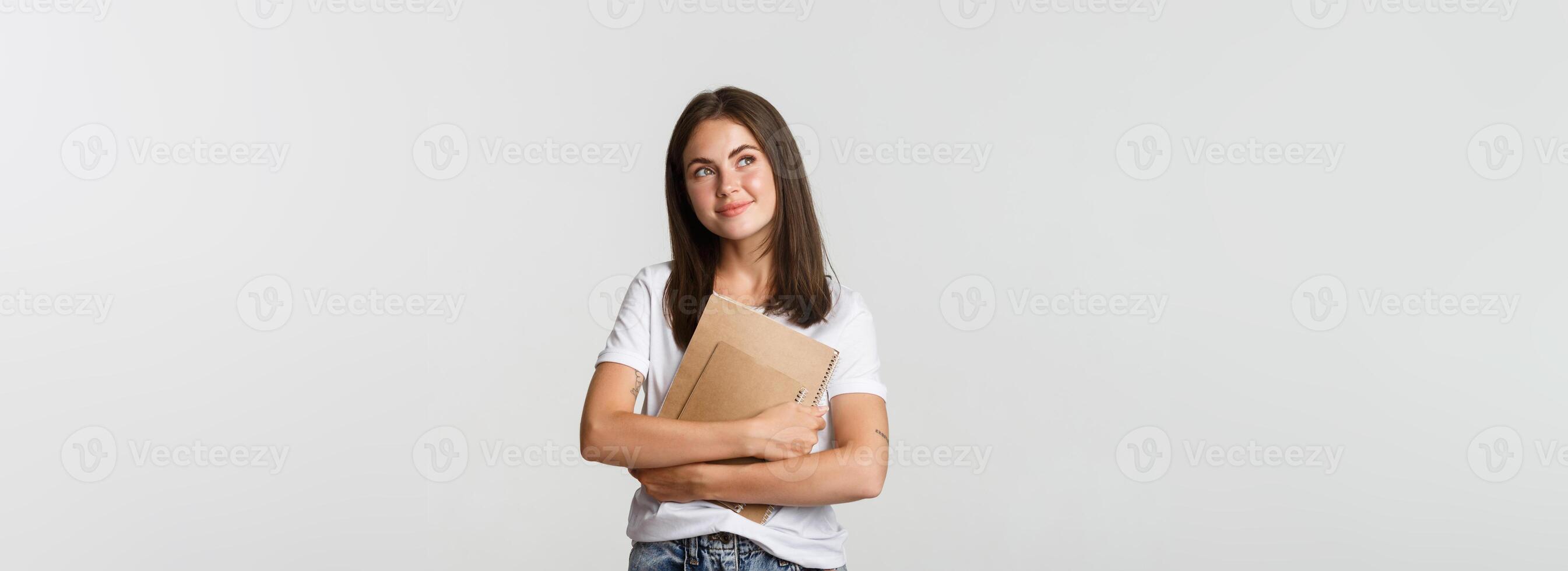Portrait of smiling nostalgic female student looking upper left corner, holding notebooks photo