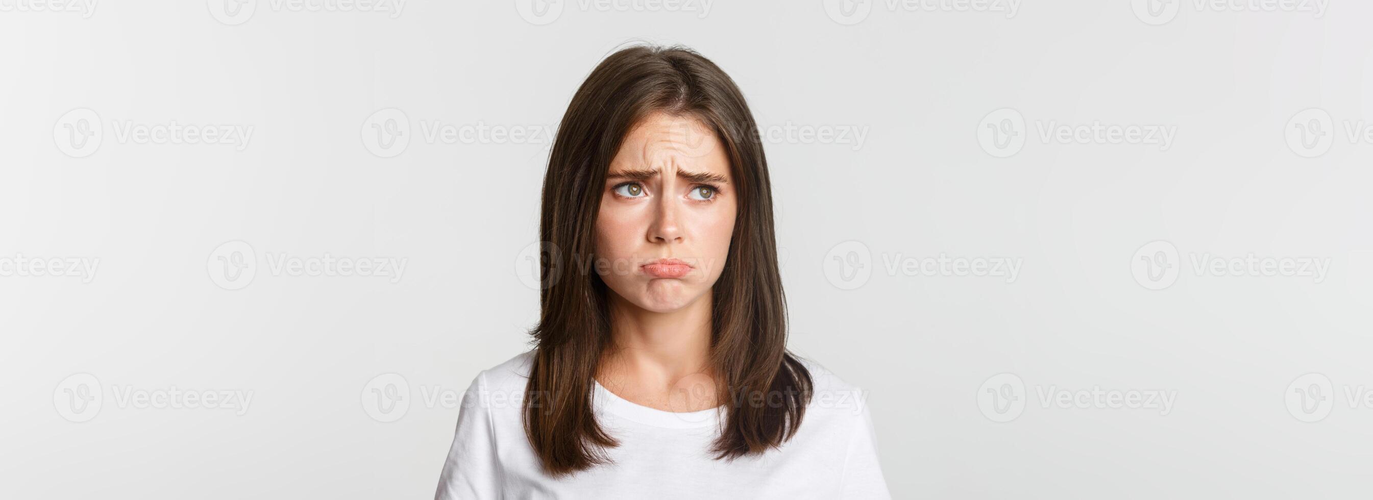 Close-up of sulking upset cute girl looking upper left corner with jealousy, standing sad over white background photo