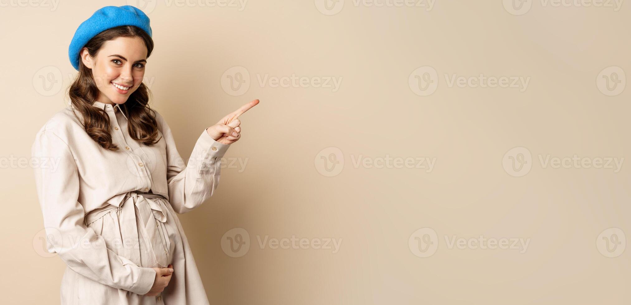 Young future mother, pregnant woman smiling, posing with big belly third trimester of pregnancy, looking happy, expecting baby, pointing right at logo, banner or advertisement photo
