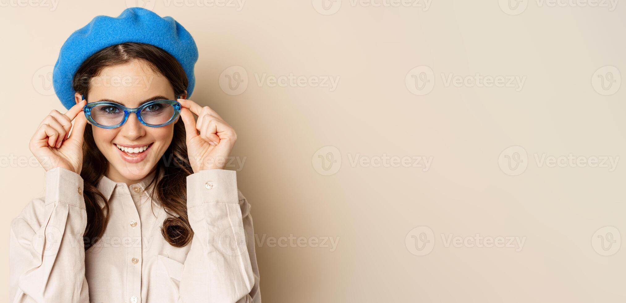 Close up portrait of stylish woman posing in sunglasses, laughing and smiling, wearing trendy outfit, standing over beige background photo