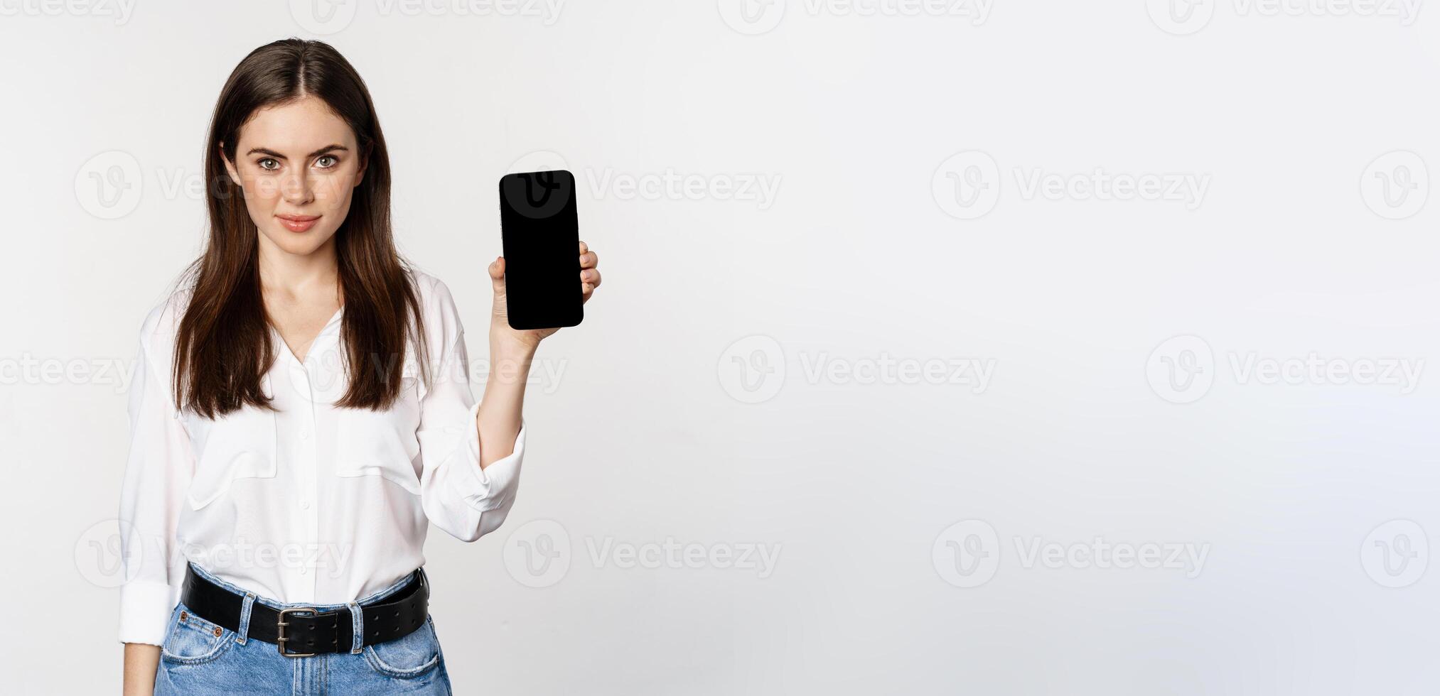 Confident woman in corporate clothes, showing smartphone screen, mobile interface of an application, standing over white background photo