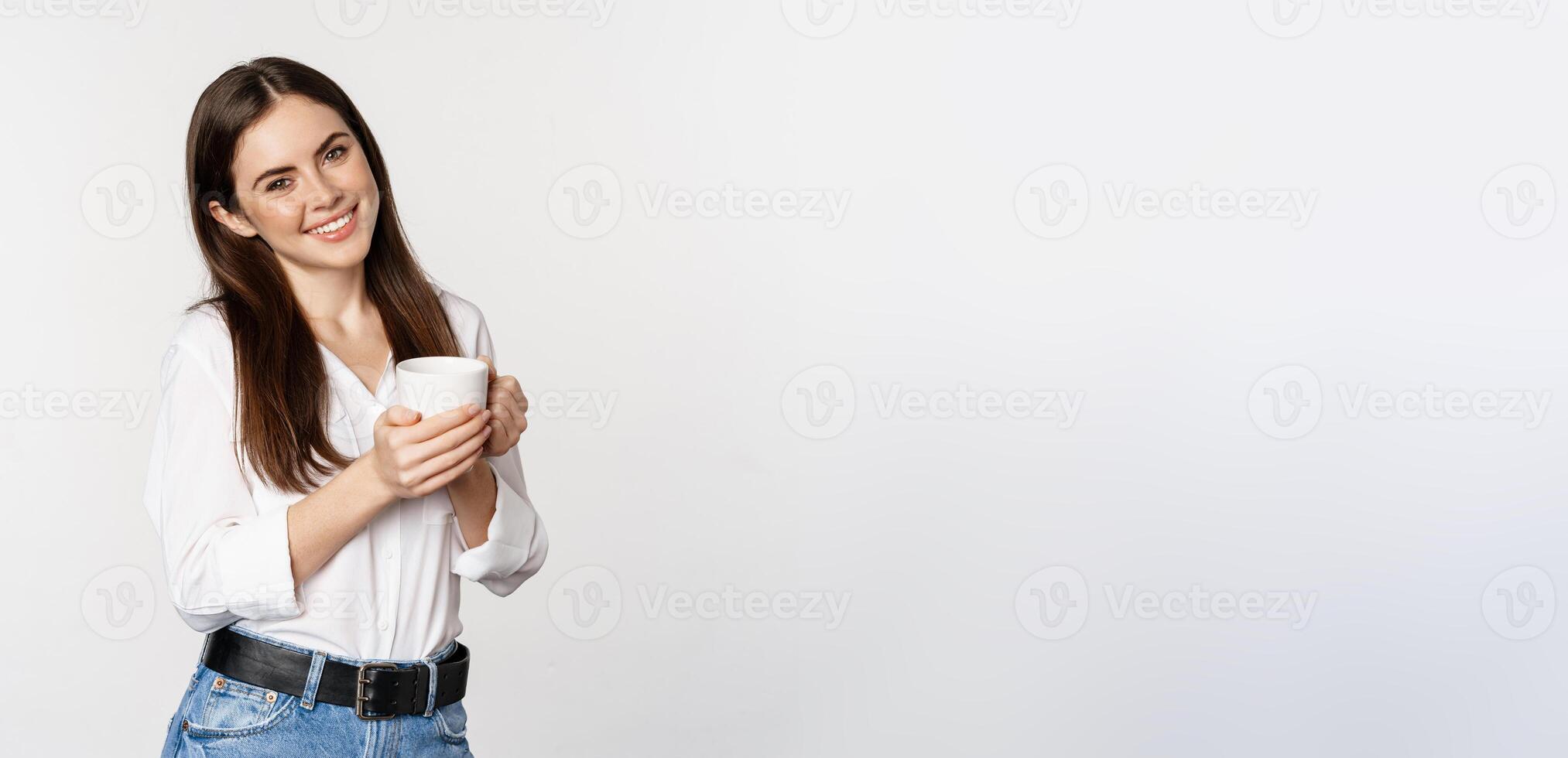 Corporate woman standing with coffee tea mug and smiling, drinking from cup, standing happy against white background photo