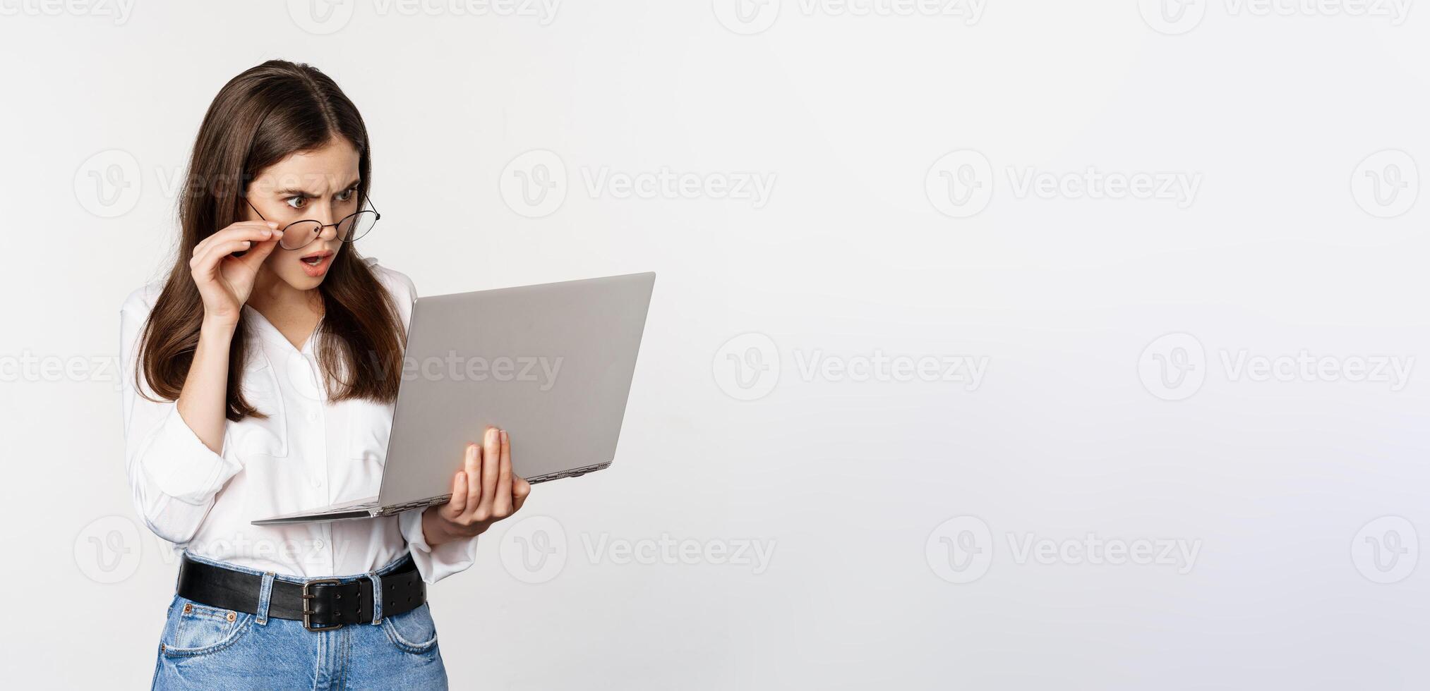 Shocked woman looking at laptop screen confused, stunned about smth on computer, standing over white background photo