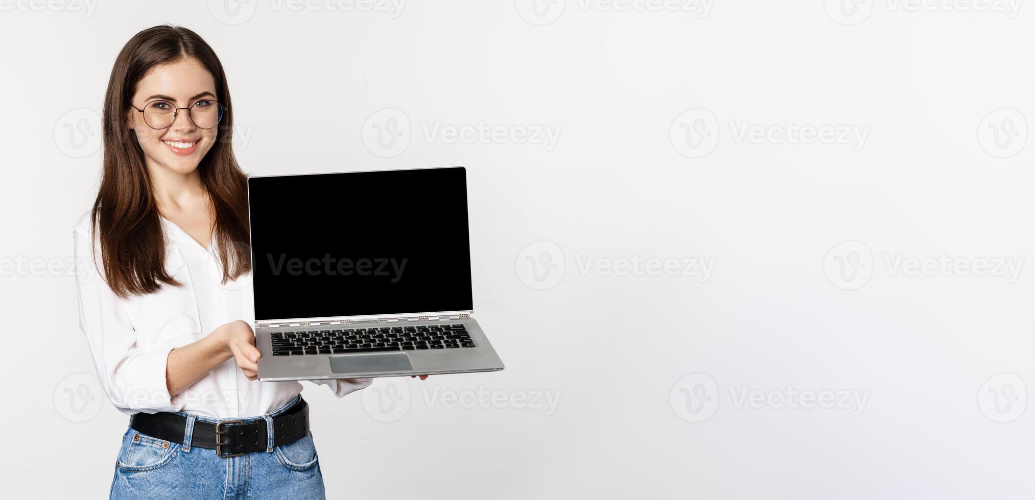 Portrait of smiling woman in glasses showing laptop screen, demonstrating company website, promo offer, standing over white background photo