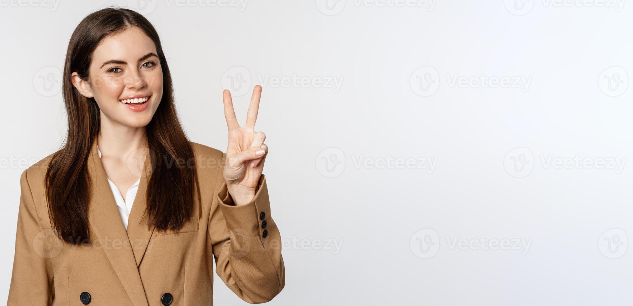 Portrait of corporate woman, saleswoman showing number two fingers and smiling, standing in suit over white background photo