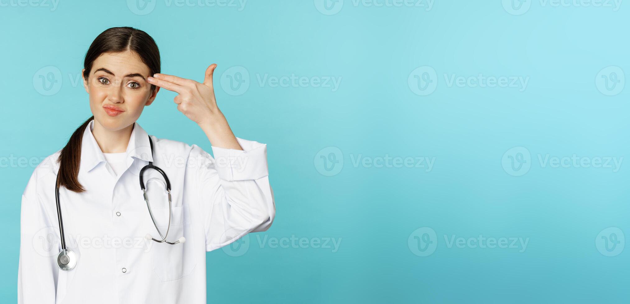 Tired and annoyed young woman showing pictol shot gesture over head, looking upset or disappointed, standing over torquoise background photo