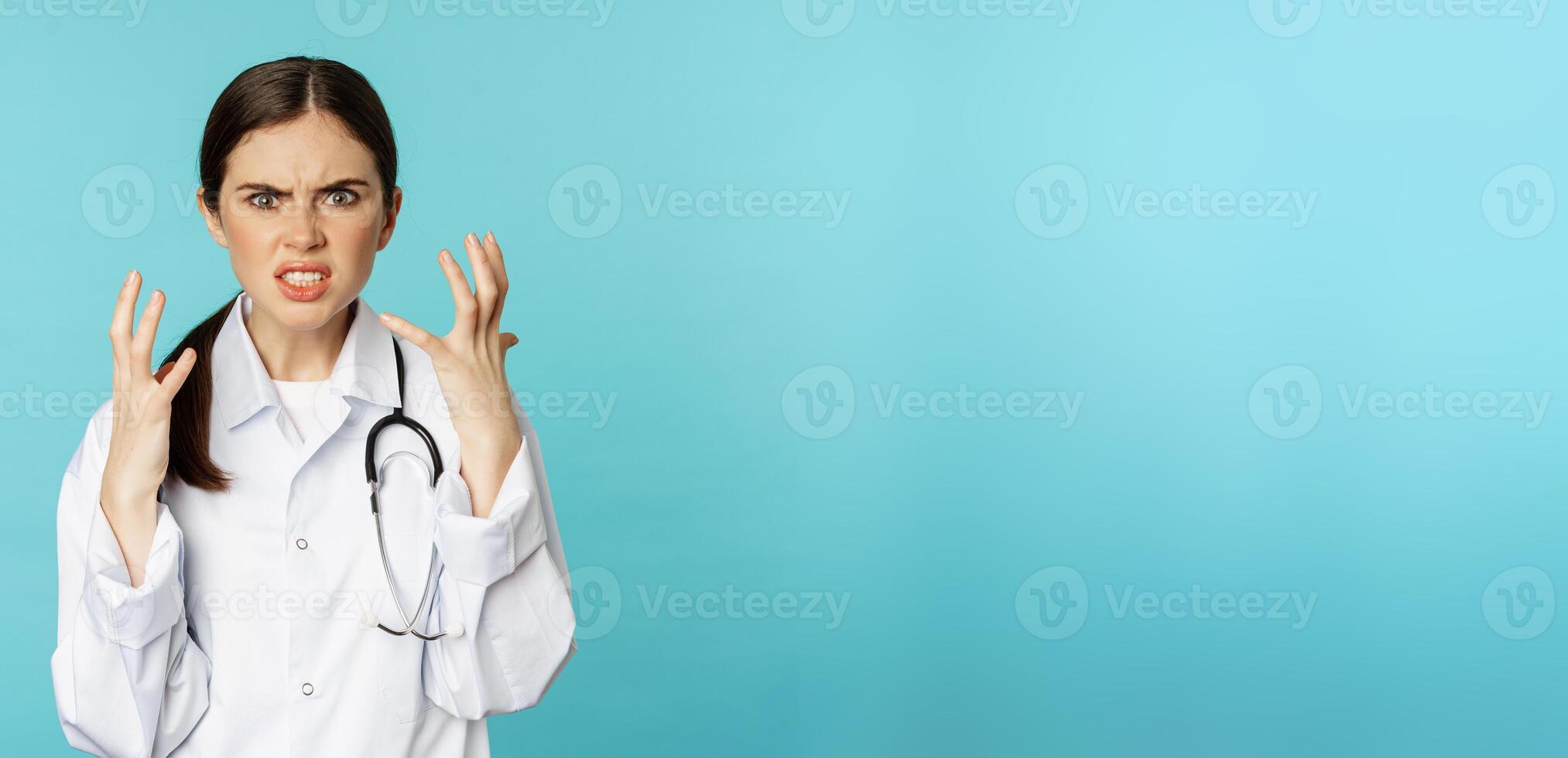 Angry and outraged woman shaking hands, cursing and looking furious, standing annoyed against torquoise background photo
