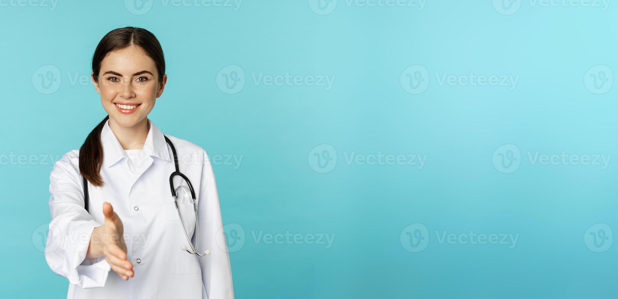 Smiling professional woman doctor, therapist extending hand, handshake gesture, greeting patient in medical clinic or hospital, standing over blue background photo