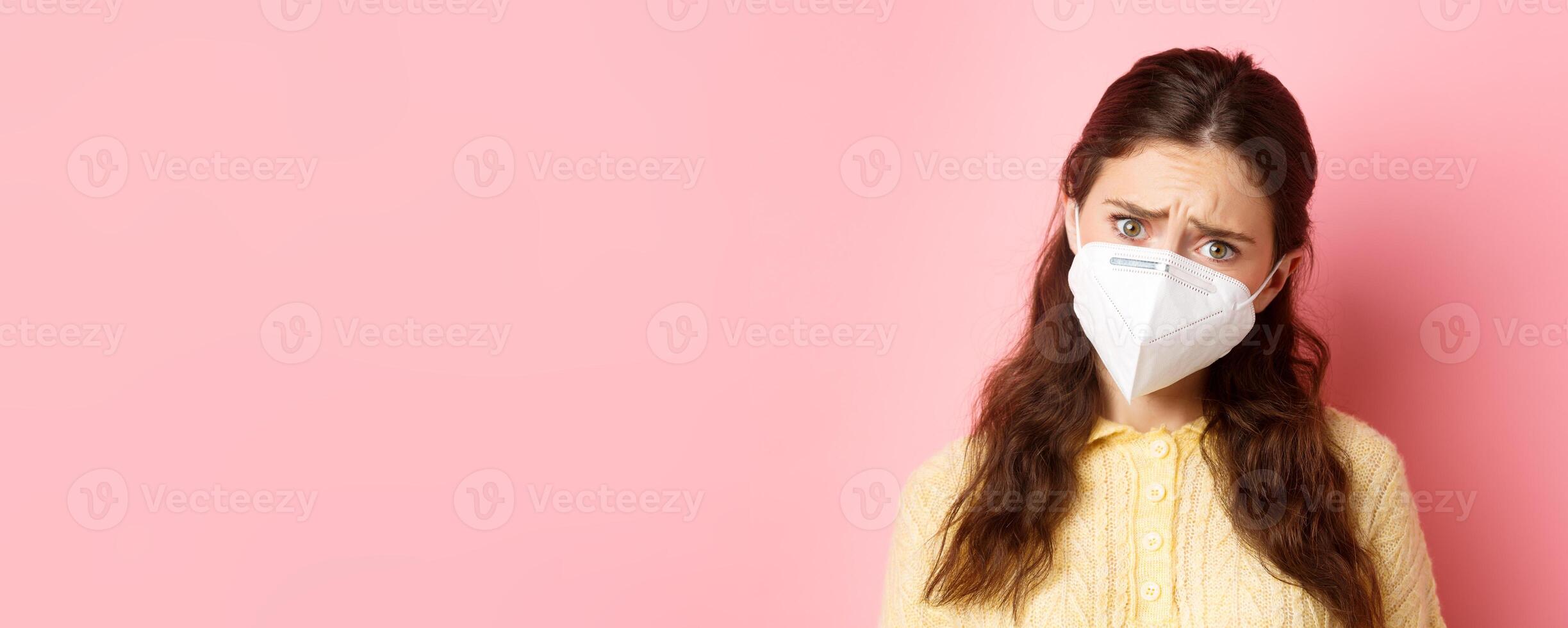 Preventive measures, health care concept. Close up of sad young woman in medical respirator express compassion, look with pity and upset face, standing against pink background photo