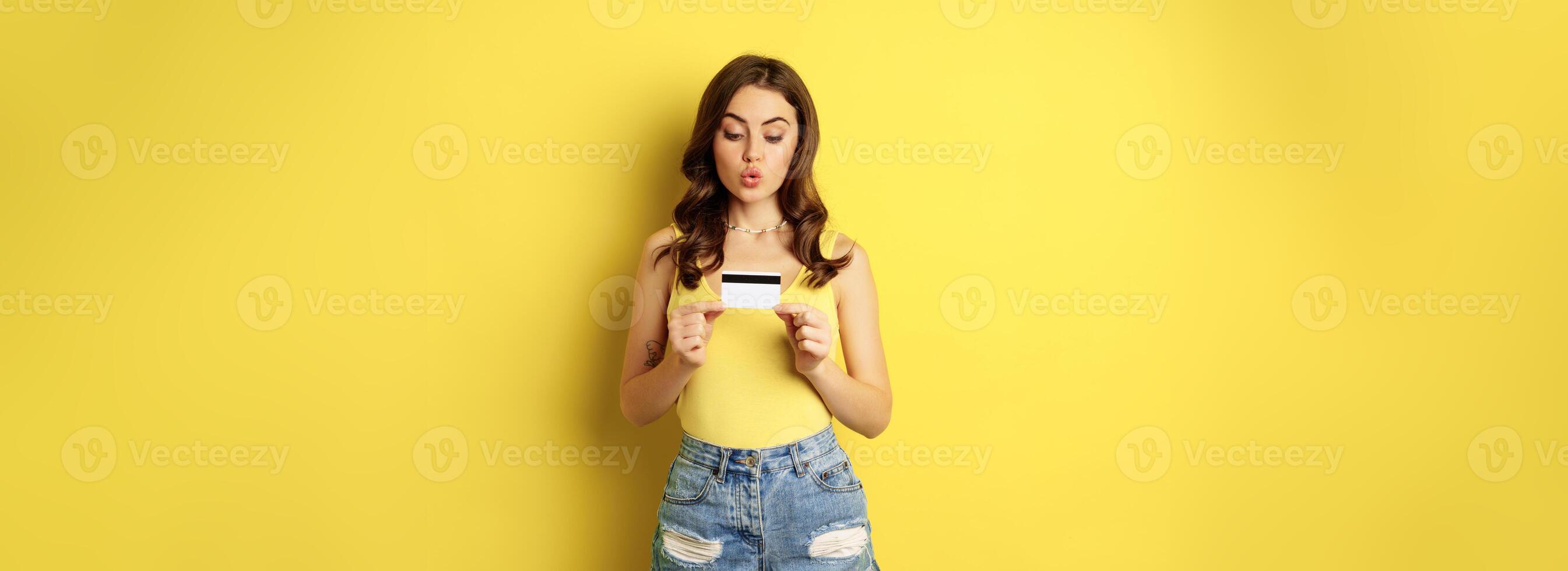 Enthusiastic young woman showing credit card, recommending bank, discount in store, contactless payment or cashback, standing over yellow background photo