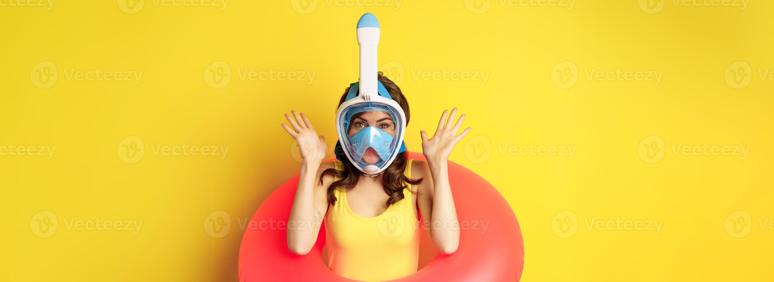 Funny happy woman in swimming ring, wearing snorkling mask for diving, posing against yellow background photo