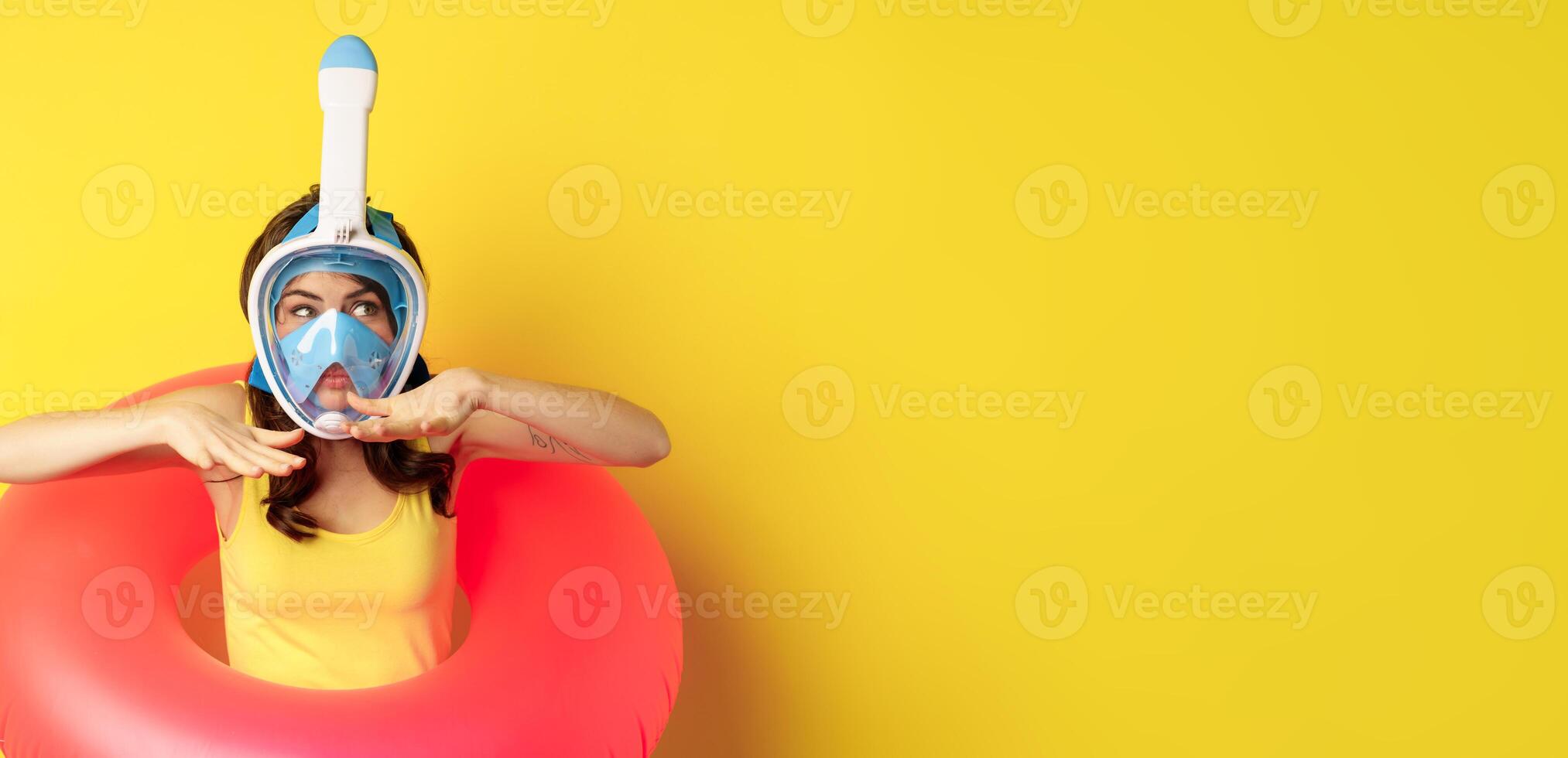 Beautiful girl in diving mask, going snorkling, wearing swimming ring, showing swim motion, standing over yellow background photo