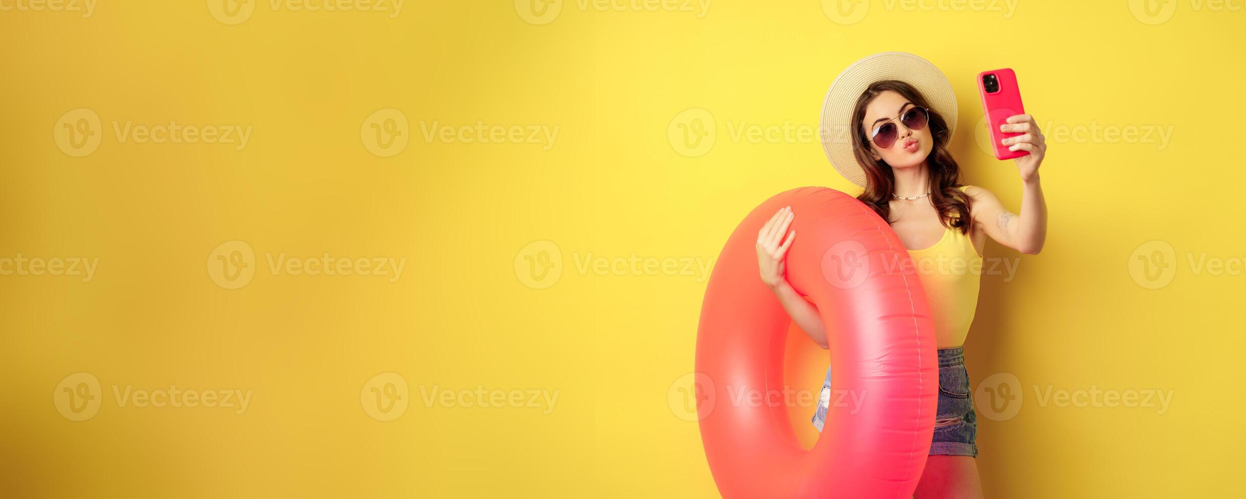 Stylish brunette girl on vacation, taking selfie with swim ring, going on beach, swimming in sea on summer holiday, standing over yellow background photo