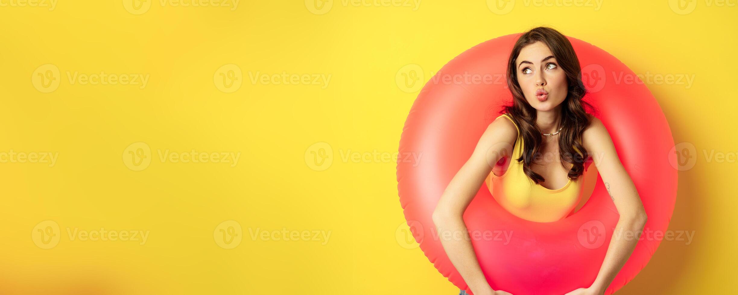 Close up portrait of coquettish young sexy woman inside pink swimming ring, concept of beach holiday, vacation and summer, yellow background photo