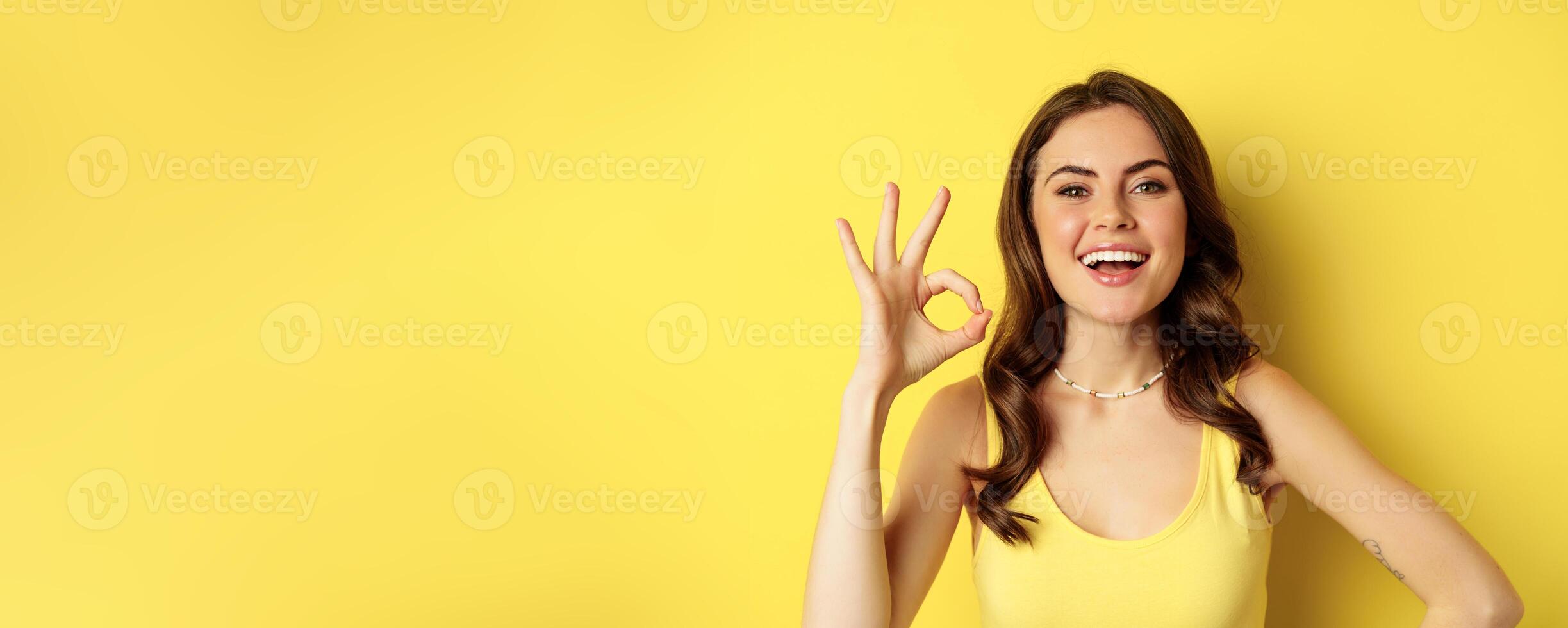 Close up portrait of young happy pretty woman, laughing and smiling with white teeth, showing excellent, okay ok sign, praise and compliment smth, yellow background photo
