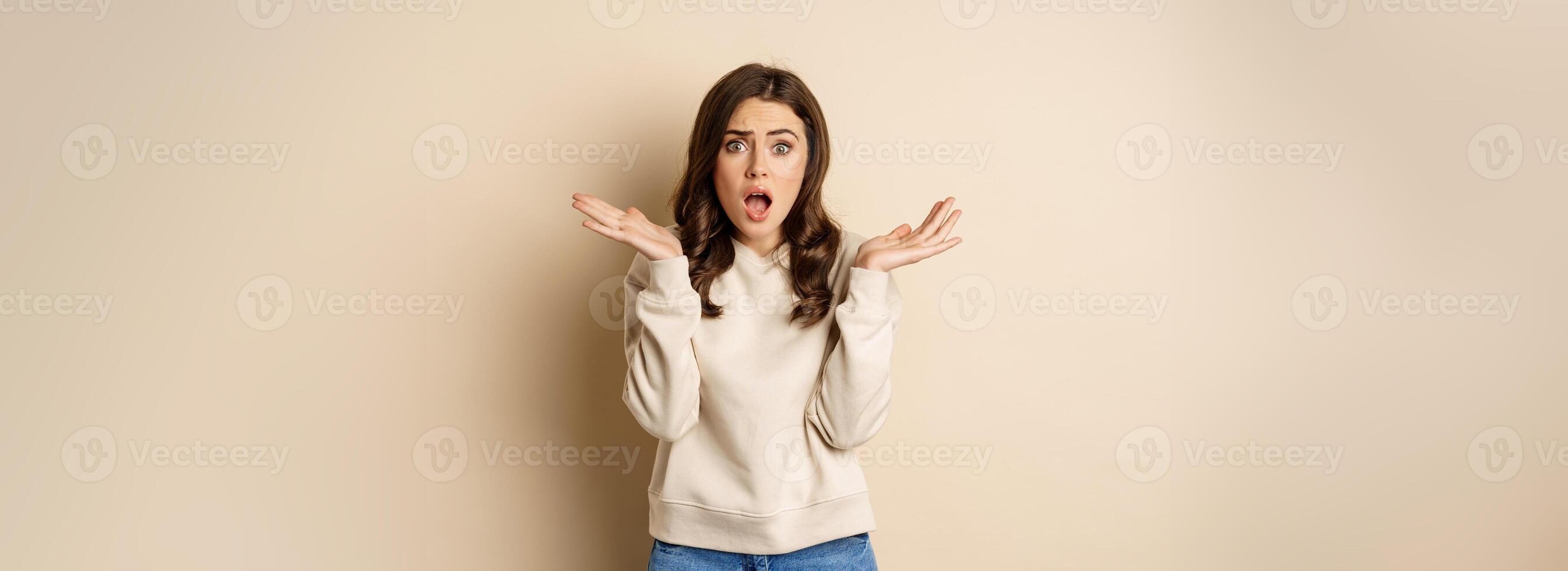 Shocked girl looking startled at camera, drop jaw and spread hands sideways in questioned and stunned face expression photo