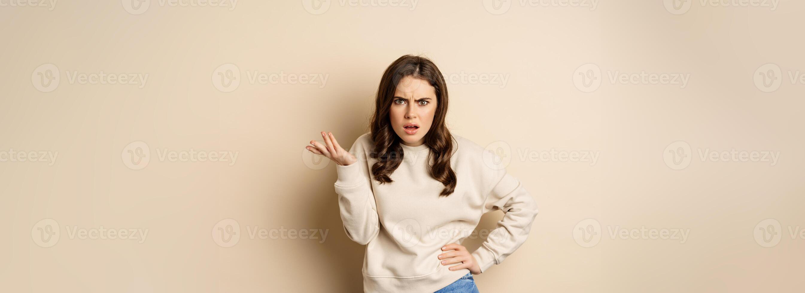 Frustrated and pissed-off woman, looking confused, arguing, standing over beige background photo