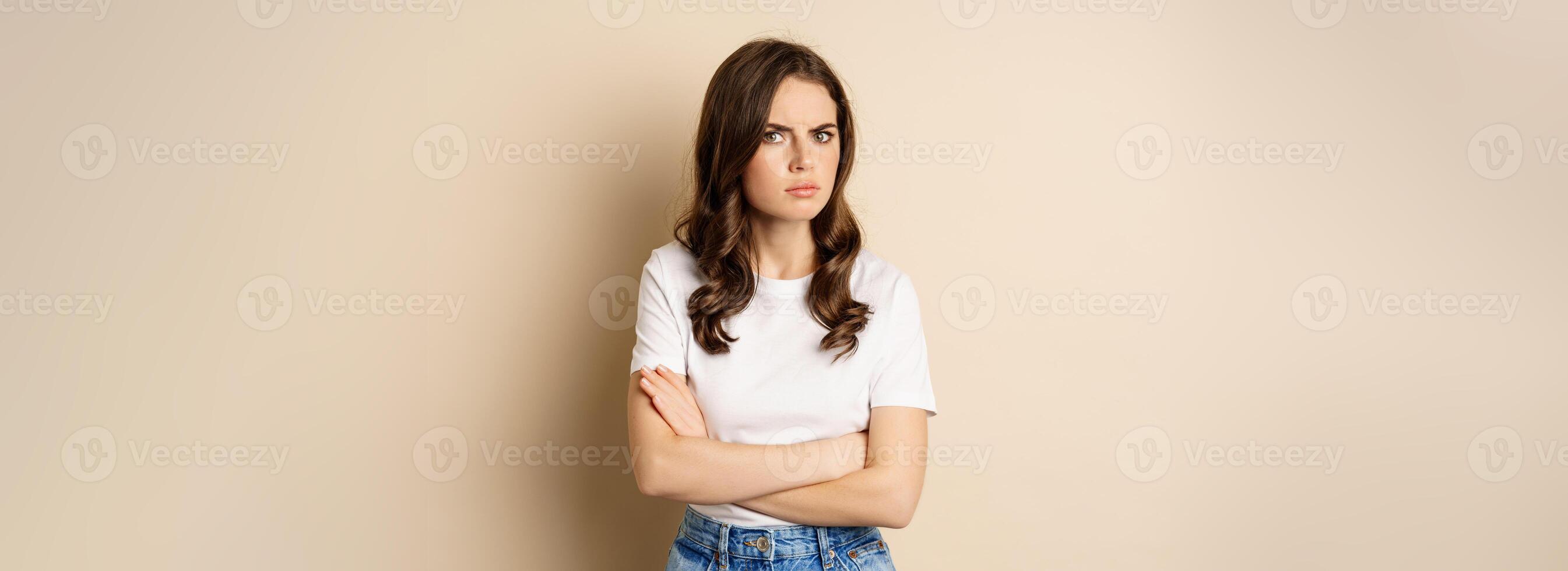Offended angry woman cross hands on chest, frowning and sulking insulted, standing over beige background photo
