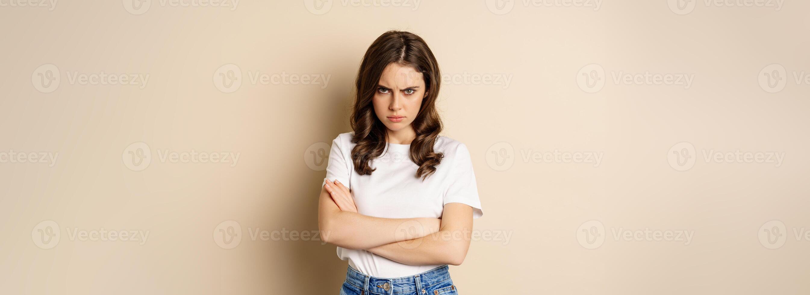 Offended angry woman cross hands on chest, frowning and sulking insulted, standing over beige background photo