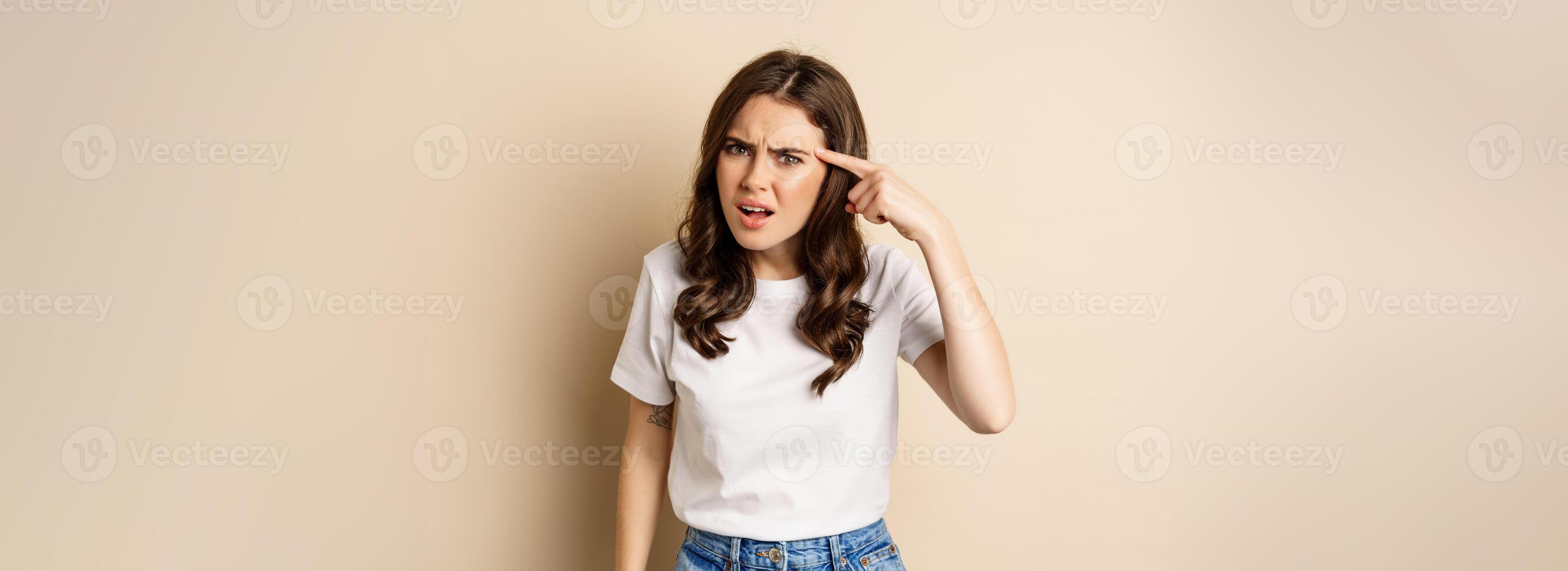 Annoyed and angry woman pointing finger at head, scolding someone, standing over beige background photo
