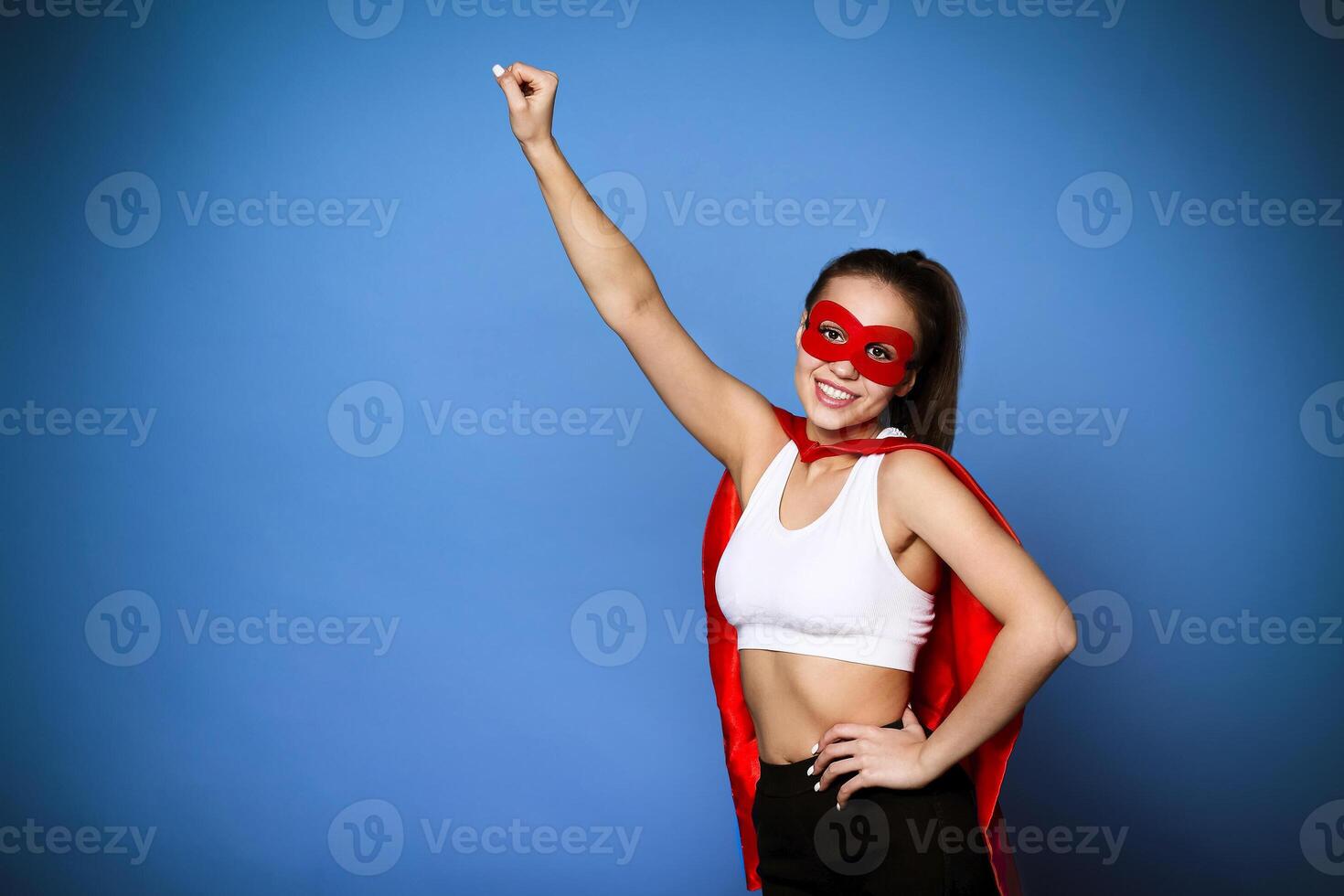 Cheerful woman in superhero cloak holding arm raised photo
