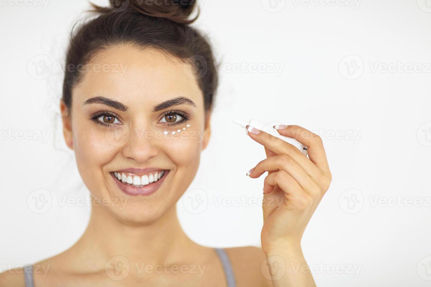 Young woman applying eyes cream on perfect skin photo