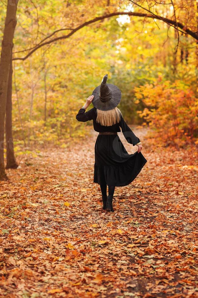 Unrecognizable witch walking in autumn forest photo