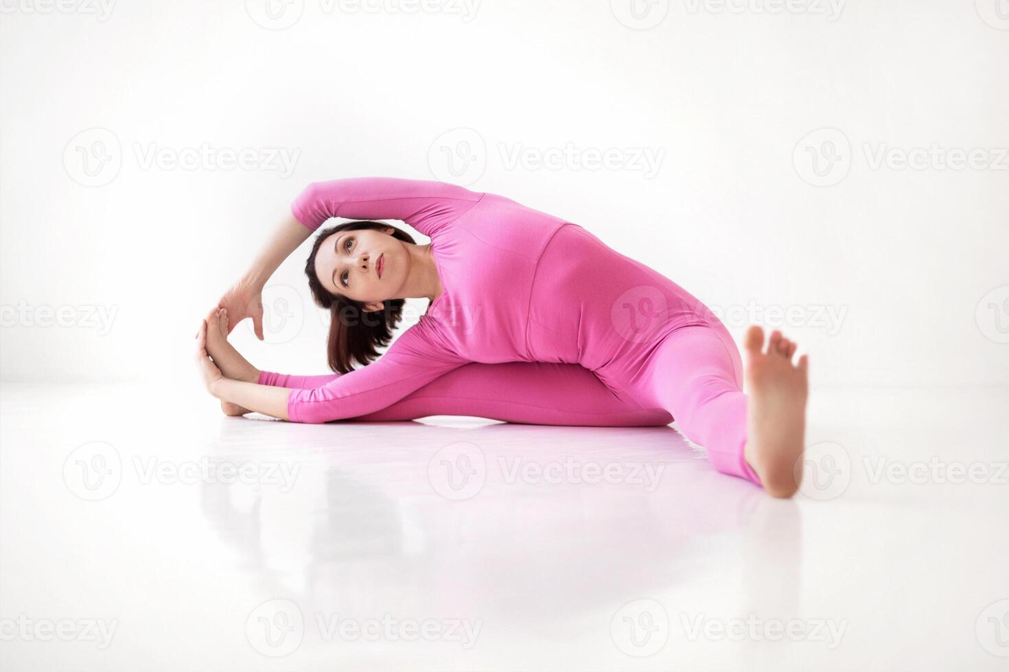 Young slender fit woman in pink long bodysuit performing yoga pose, isolated over white studio background photo