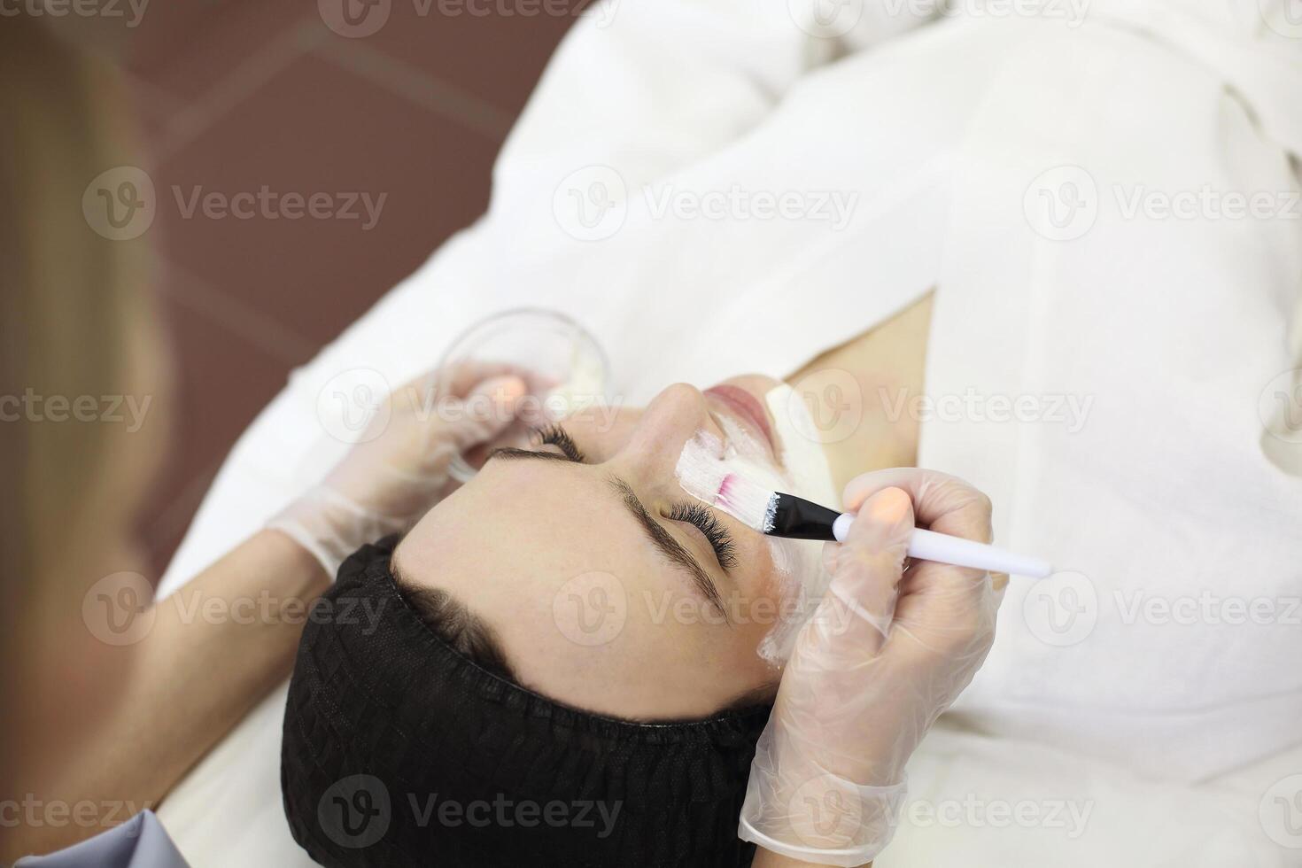 Crop cosmetologist applying facial mask on client photo